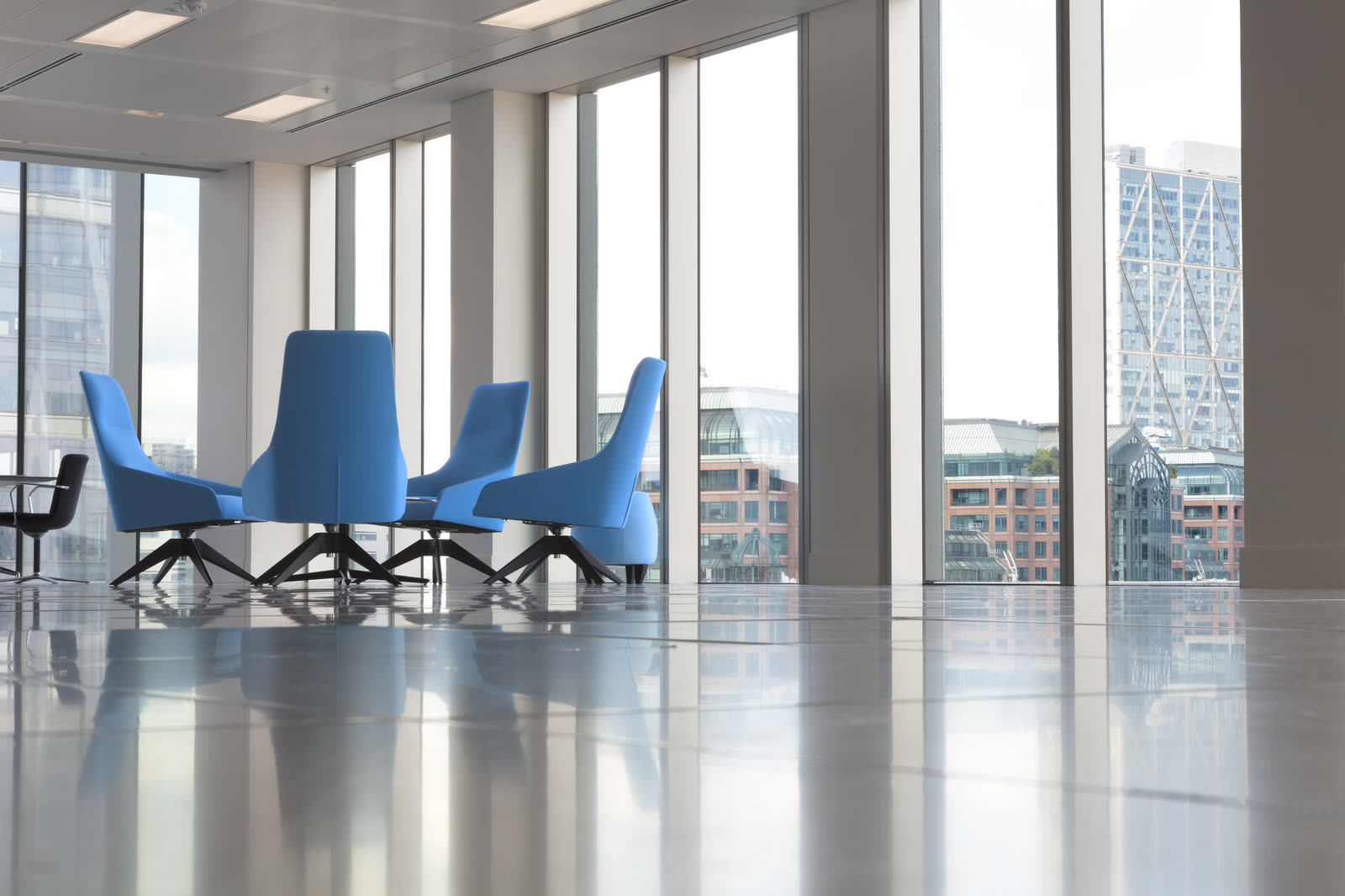 Sunlit modern office lounge with blue armchairs and floor-to-ceiling windows
